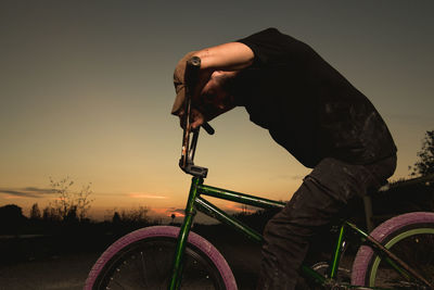 Side view of man riding bicycle against sky during sunset