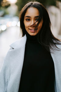 Modern ethnic female in trendy coat and with bag walking on pedestrian street and looking at camera