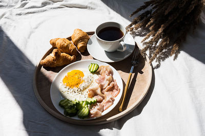 Breakfast in bed coffee cup, fried egg, bacon and croissants on wooden tray. 