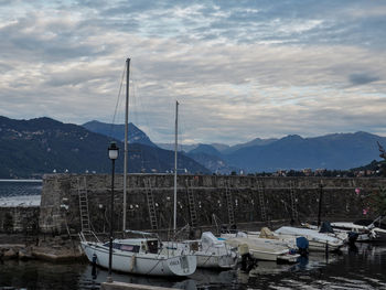 Sailboats moored at harbor against cloudy sky