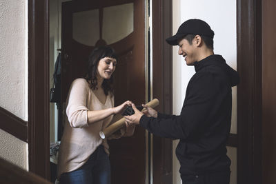 Smiling customer talking to delivery man while signing on smart phone at doorstep