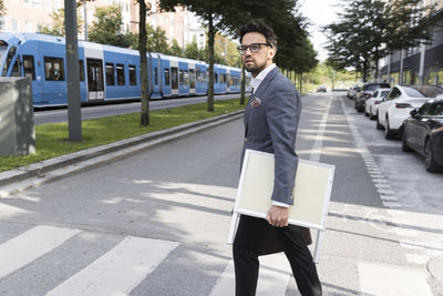 Side view of male real estate agent carrying placard while crossing street