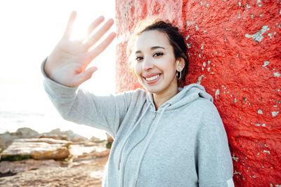 Portrait of young woman with arms raised standing against wall