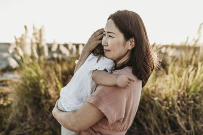 Mid view of happy mom embracing young toddler at beach during sunset