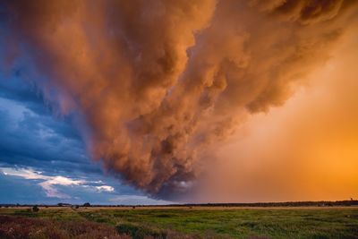 Scenic view of landscape against dramatic sky during sunset