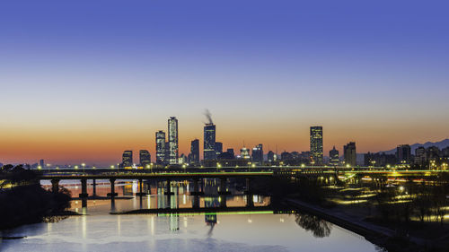 Illuminated buildings in city against clear sky during sunset