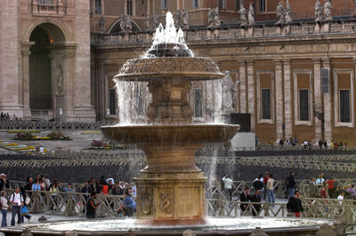 People walking by fountain against st peter basilica