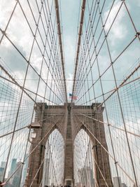 Low angle view of suspension bridge against cloudy sky