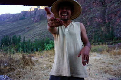 Laughing man wearing hat while gesturing against mountains