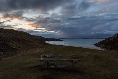 Empty bench on shore by sea against sky