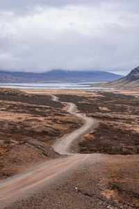 Scenic view of empty road amidst landscape at eastfjords against cloudy sky