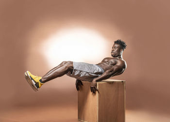 Full length of shirtless athlete exercising against brown background