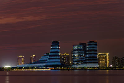 Illuminated modern buildings in city against sky at night