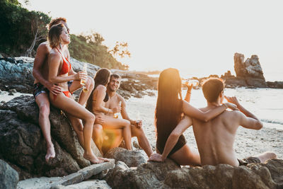 People sitting on rock at beach against sky