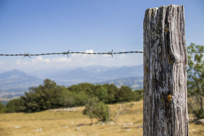 Barbed wire fence on field against scenic background