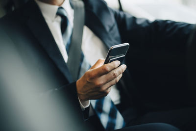 Midsection of businessman using smart phone sitting in taxi