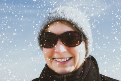 Portrait of smiling woman wearing sunglasses during snowfall
