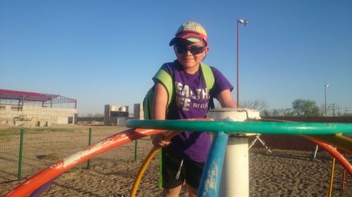 Full length of happy boy standing on playground against clear blue sky