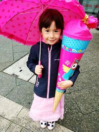 Happy girl holding pink umbrella while standing on road