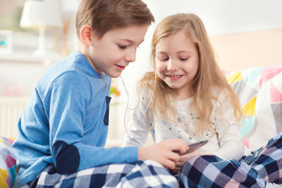 Boy with sister using phone on bed at home