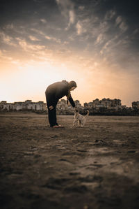 Side view of young woman playing with cat on field at sunset