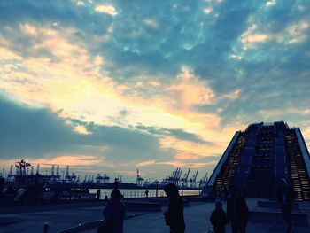 Silhouette of people walking on bridge against cloudy sky