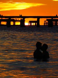 Silhouette couple in sea against orange sky