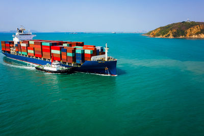 Container ship sailing in green sea and tugboat drag and blue sky background from drone shot