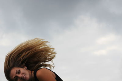 Side view of woman tossing hair against cloudy sky