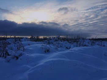 Snow covered landscape against sky during sunset