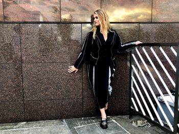 Full length of young woman standing against wall at building terrace