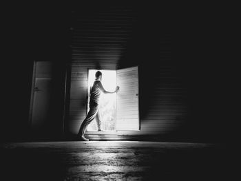 Side view of young man standing at doorway in darkroom