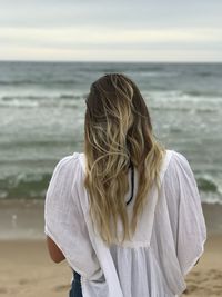 Rear view of woman walking at beach against sky