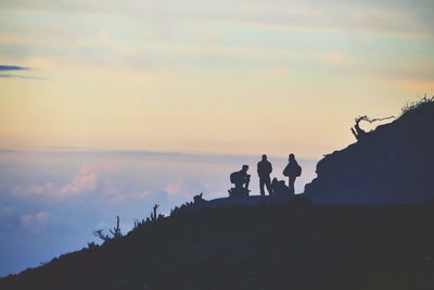 Silhouette people standing on rock against sky during sunset
