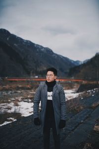 Portrait of young man standing on mountain against sky