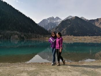Female friends walking at lakeshore against mountains