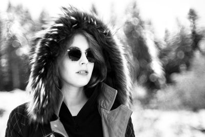 Portrait of woman with sunglasses against trees in winter