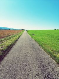 Road amidst field against clear sky