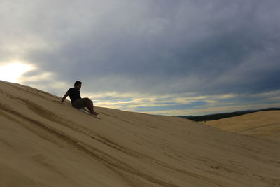 Man on sand dune in desert against sky