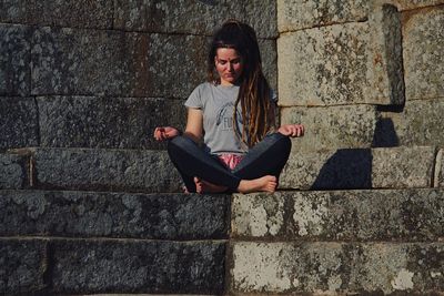 Portrait of a young woman sitting against wall