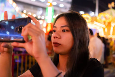 Young woman photographing at amusement park at night