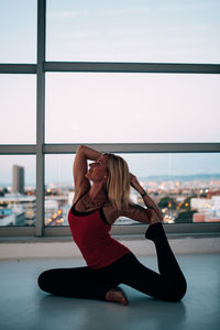 Full length of woman wearing hat while sitting on window