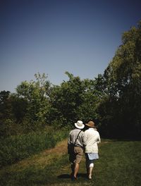 Rear view of friends walking on field against trees