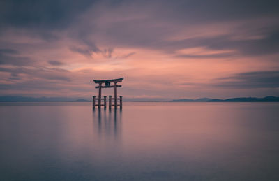 Silhouette wooden posts in lake against sky during sunset