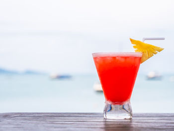 Red drink in glass on table against sea