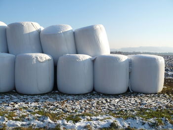 Covered hay bales on farm during winter against clear sky