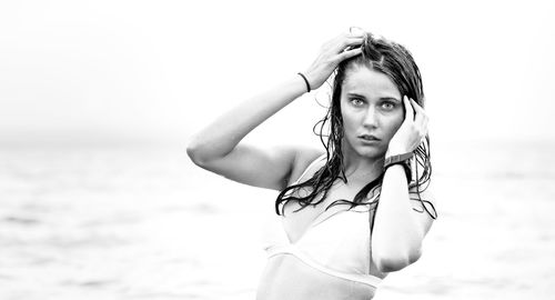 Portrait of young woman standing at beach against sky