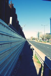 Road amidst buildings against clear blue sky