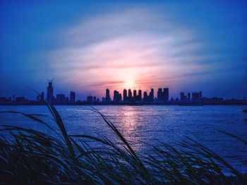 Silhouette buildings by sea against sky during sunset