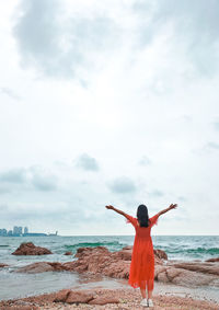 Rear view of woman standing with arms outstretched at beach